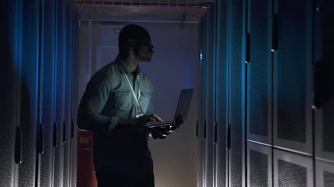 Engineer works in dark server room black man with laptop Stock Footage 163813977