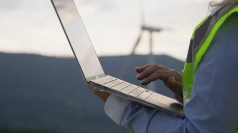 An engineer works with a laptop in the background of a wind farm, developing the Stock Footage 270990843