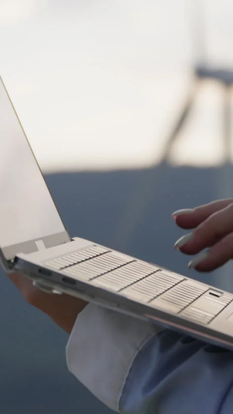 An engineer works with a laptop in the background of a wind farm, developing the Stock Footage 272312872