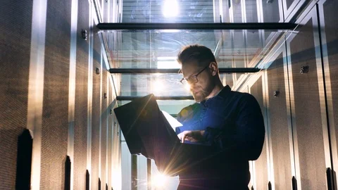 Engineer works in a server room, typing on a laptop. Computer system security Stock Footage 111875220