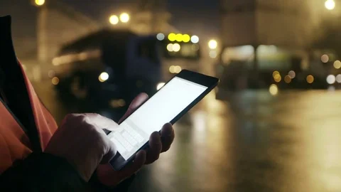 Engineer works on tablet computer and watches at big trucks at heavy industry Видео 69828316