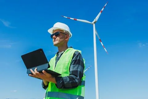 Engineer works with tablet near wind turbine at renewable energy site on a .. Foto stock
