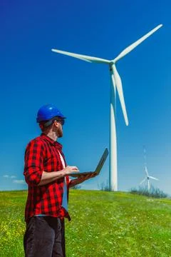 Engineer works on wind turbine project with laptop in field surrounded by w.. Foto stock