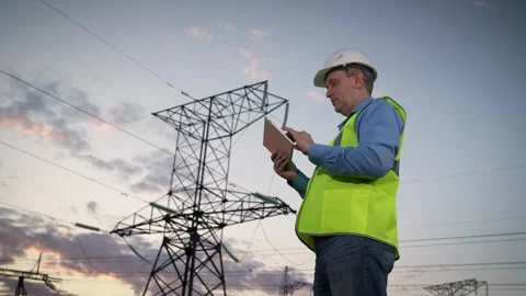 Engineer writes report on tablet looking at power transmission lines in field Stock Footage 252647330