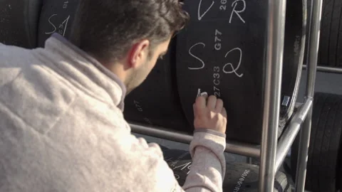 Engineer writing on race tires stacked on trolley, formula 1, racing Stock Footage 135300690