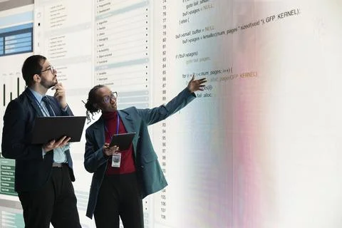 Engineering team reviews source code on digital display using laptop Stock Photos