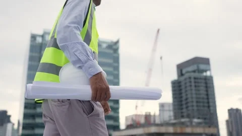 Engineerman in a yellow vest is holding a stack of blueprints while walking.. 動画素材 280732576