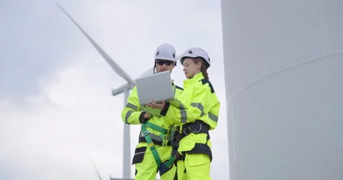 Engineers in bright safety uniform analyzing data on laptop under wind turbine, Stock Footage 330761946