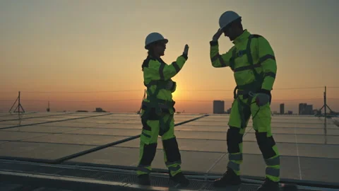 Engineers celebrating successful solar panel installation on a rooftop at sunset 스톡 동영상 339649732