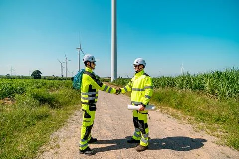 Engineers collaborating at a wind farm while reviewing project plans under .. Stock Photos