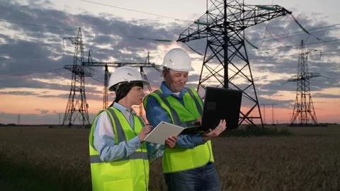 Engineers with colleague study data on computers by power transmission lines Stock Footage 270209611