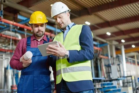 Engineers in hard hats looking at the screen of a tablet. Stock Photos