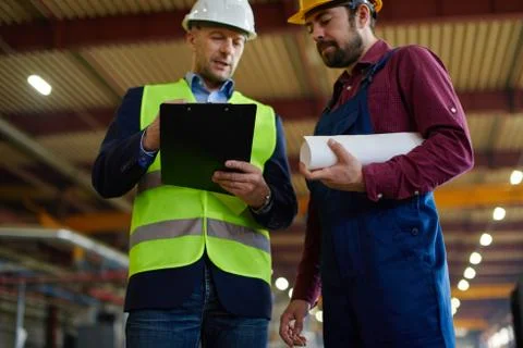 Engineers in hard hats work on changing a folded blueprint one of them holds. Foto stock