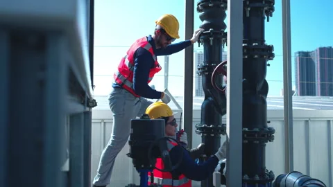 Engineers inspecting industrial pipeline and valve systems on a building rooftop 스톡 동영상 339644341