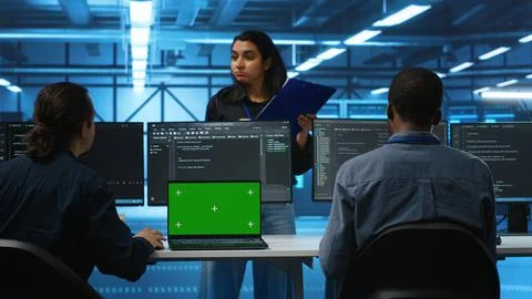 Engineers at PC desk overseeing server clusters using chroma key notebook Foto stock