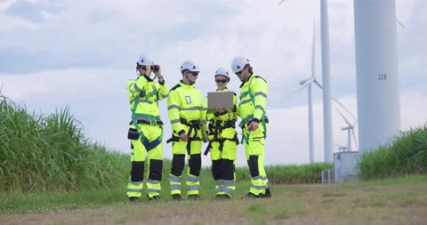 Engineers standing together near wind turbine reviewing maintenance plan with Stock Footage 321047533