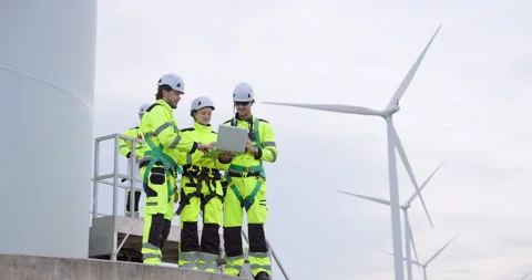 Engineers standing on turbine base platform reviewing project data on laptop, Stock Footage 330761975