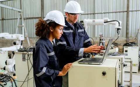 Engineers technicians controlling robotic arms on computer laptop at factory Stock Photos