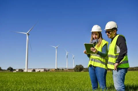 Engineers using tablet analyzing wind turbines in green field Stock Photos
