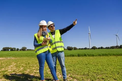 Engineers using tablet analyzing wind turbines in green field Stock Photos