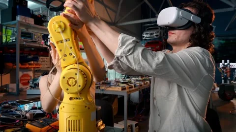 Engineers wearing vr headsets working on yellow robotic arm in tech laborator Stock Footage 339346869