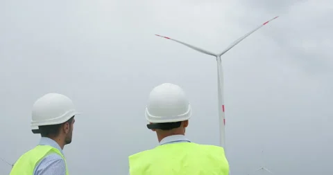 Engineers in white helmets look at operating wind turbine Stockbeeldmateriaal 160648107