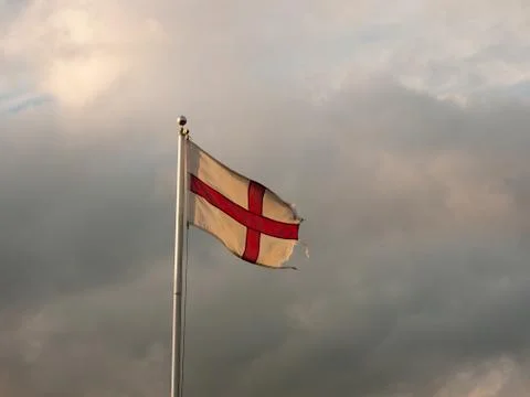 England flag flying with cloudy dramatic skies during sunset Stock Photos