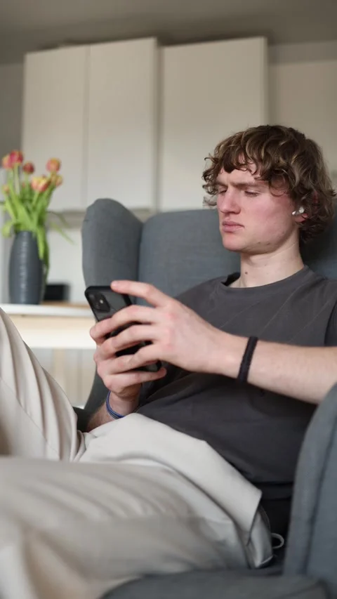 English: Vertical screen: Suspicious young man holding smartphone, looking doubt Stock Footage 302632370