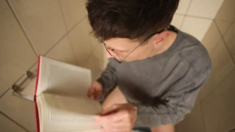 Engrossed reader on the toilet. A man gets so absorbed in an interesting book Stock Footage 303474168