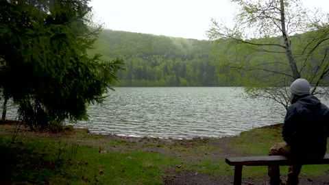 Enigmatic lonely man sitting on bench on lake shore in the mountain forest. Stock Footage 150593390