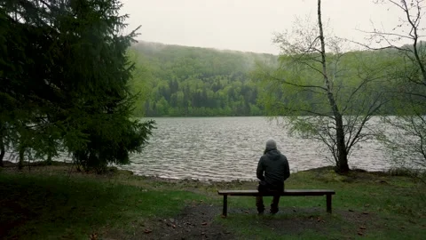 Enigmatic lonely man sitting on bench on lake shore in the mountain forest. Video stock 150593491