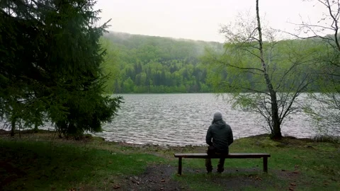 Enigmatic lonely man sitting on bench on lake shore in the mountain forest. 스톡 동영상 150593532