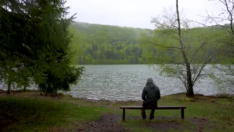 Enigmatic lonely man sitting on bench on lake shore in the mountain forest. Stock Footage 150593636