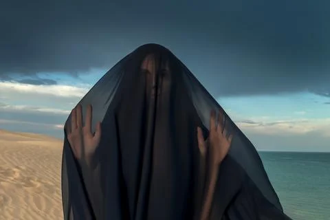 Enigmatic Veiled Figure on Desolate Beach: Mysterious Dark Presence Against.. Foto stock