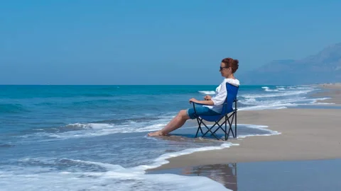 Enjoy the waves while sitting in a chair by the ocean Stock Footage 297713932