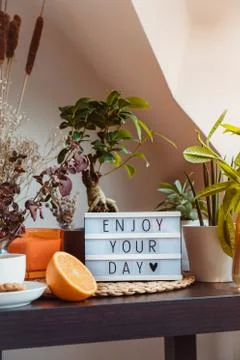 Enjoy your day message on lightbox standing on a table with cup of tea and green Foto stock