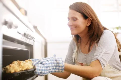 Enjoying the aroma of her fresh scones. A mature woman taking scones out from Stock Photos