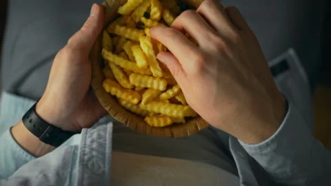 Enjoying a bowl of crispy fries while relaxing on a cozy couch in the evenin Stock Footage 300389598