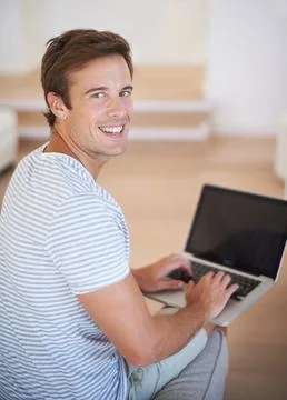 Enjoying broadband connectivity. A young man working on a laptop and smiling at Stock Photos