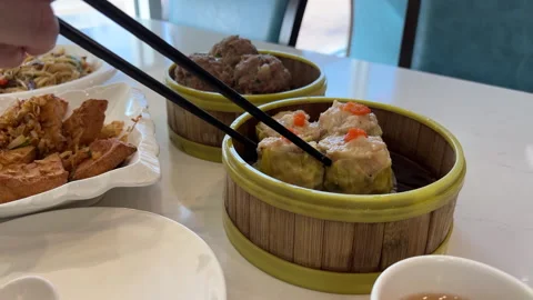 Enjoying Dim Sum: Man Picking Up Siomai with Chopsticks at Restaurant Table Stock Footage 295783601