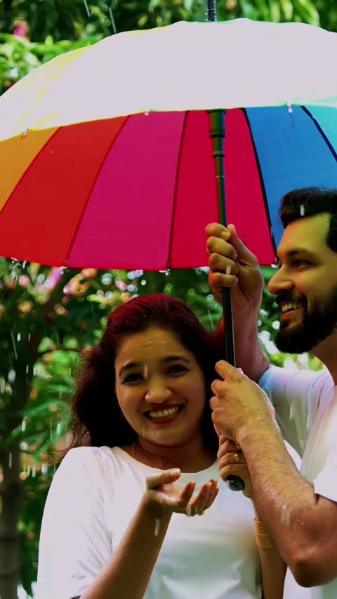 Enjoying first rain shower, Indian couple having fun under umbrella in park Stock Footage 343163987