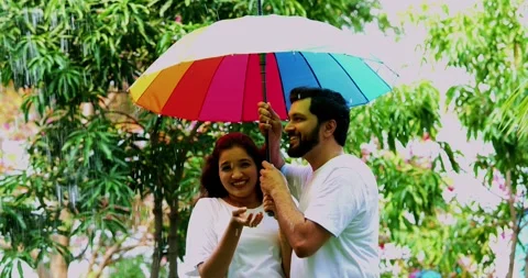Enjoying first rain shower, Indian couple having fun under umbrella in park Stock Footage 343164640