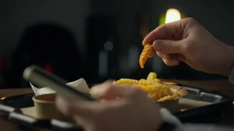 Enjoying fresh fries while using a smartphone at a cozy venue during the eve Stock Footage 305342673