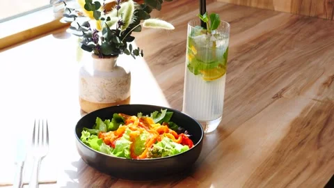 Enjoying a Fresh Salad and a Refreshing Mojito in a Bright and Inviting Cafe Stock Footage 311874080