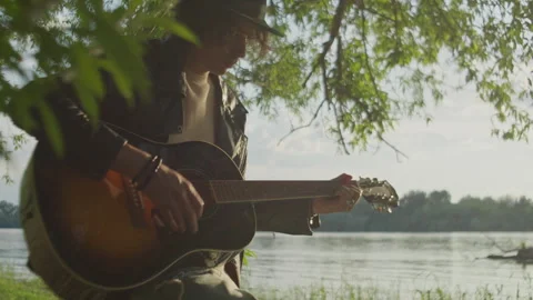 Enjoying nature while playing strumming man guitar by the water Stock Footage 319950544