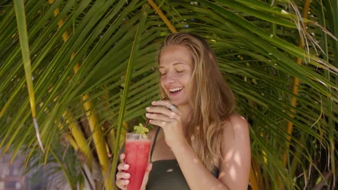 Enjoying a refreshing watermelon drink under palm trees on a sunny beach day Stock Footage 293106776