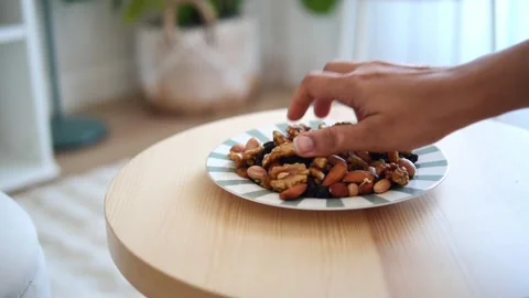 Enjoying a snack of mixed nuts at home on a wooden table Stock Footage 333943090