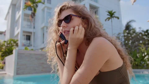 Enjoying a sunny afternoon by the pool while talking on the phone in a tropical Stock Footage 296716955