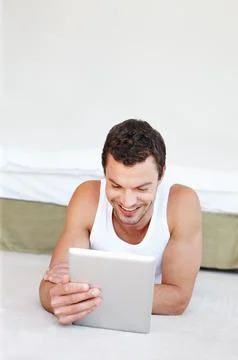 Enjoying touchscreen technology. A handsome man lying on his bed working on his Stock Photos