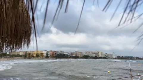 Enjoying a Tranquil Beachfront View With a Thatched Roof on a Cloudy Day by the Stock Footage 296106150
